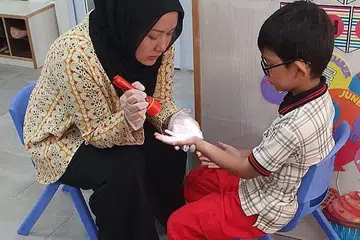 USAHA CEGAH PENULARAN VIRUS WUHAN: Pembantu guru, Cik Nurshahdilla Talib, memeriksa kesihatan dan kebersihan peribadi kanak-kanak di pusat PPIS. - Foto PPIS.