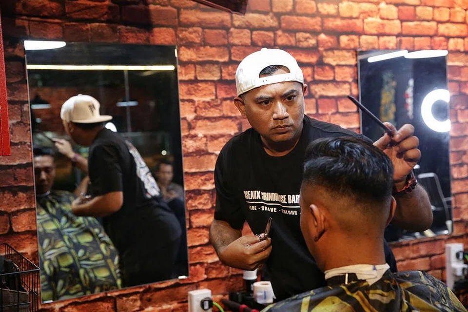 KINI DITUTUP: Pemilik Atatcutz Singapore dan Ciseaux Grindhouse, Encik Fendy Ali, menggunting rambut seorang pelanggan dalam satu foto yang diambil pada 27 Februari lalu, sebelum arahan memakai pelitup dikuatkuasa. Dua kedai gunting rambutnya kini perlu ditutup berikutan langkah lebih ketat di bawah tempoh pemutus litar. - Foto fail
