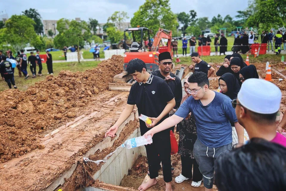 Anak Allahyarham Nur Mohammad Azmi, Encik Syafiez Nur Mohammad (kiri), dan abangnya, Encik Sofyan (kemeja T biru) semasa pengebumian bapa mereka, Allahyarham Nur Mohammad Azmi, yang dikenali sebagai Nur JM Mohd (gambar sisipan), di Pusara Aman.