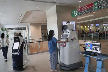 GUNAKAN ROBOT: Robot keselamatan (kiri) yang bergerak melakukan rondaan di kawasan hospital dan mengenal pasti kegiatan mencurigakan. Seorang pengunjung Hospital Besar Ng Teng Fong menunjukkan robot keselamatan dan concierge (kanan) pendaftaran SafeEntry beliau. - Foto BH oleh KELVIN CHNG