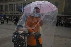 BERWASPA: Seorang wanita memakai pelitup dan menggunakan payung untuk menggantung beg plastik demi melindungi dirinya dan seorang kanak-kanak daripada koronavirus Covid-19 di stesen kereta api Beijing kelmarin. 