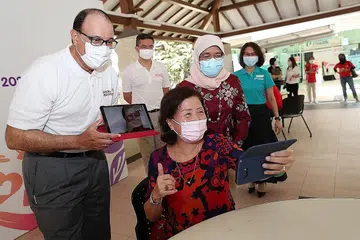 MENDAKAP GAYA HIDUP DIGITAL: (Kiri) Encik Iswaran dan Puan Halimah (kanan) berinteraksi dengan Cik Patsy Low (tengah) yang membuat panggilan video kepada ahli keluarganya. - Foto BH oleh TIMOTHY DAVID