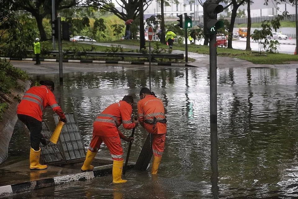 BUKA LONGKANG: Pekerja membuka penutup longkang bagi membantu pengaliran air yang dikatakan penyebab banjir di simpang Pasir Ris Drive 12 dan Tampines Avenue 10. - Foto BH oleh KEVIN LIM