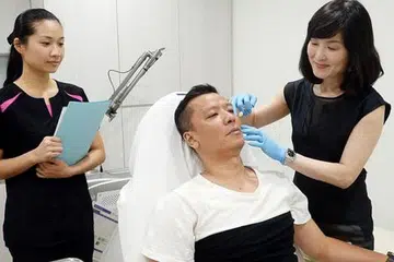 PERBAIKI KULIT: Dr Lam menunjukkan cara beliau menyuntik ubat yang digunakan bagi rawatan wajah Encik Sani bagi memperbaiki kulit mukanya itu. - Foto-foto JOHARI RAHMAT
