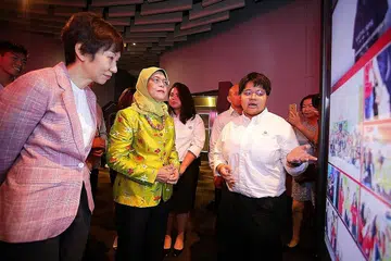 PROJEK MASYARAKAT: Cik Huril (kanan) menerangkan tentang projek masyarakatnya di bawah program kepimpinan Kor Belia Singapura (YCS) kepada Presiden Halimah Yacob dan Menteri Kebudayaan, Masyarakat dan Belia, Cik Grace Fu, di sebuah majlis menandakan tamat program itu baru-baru ini. - Foto NYC