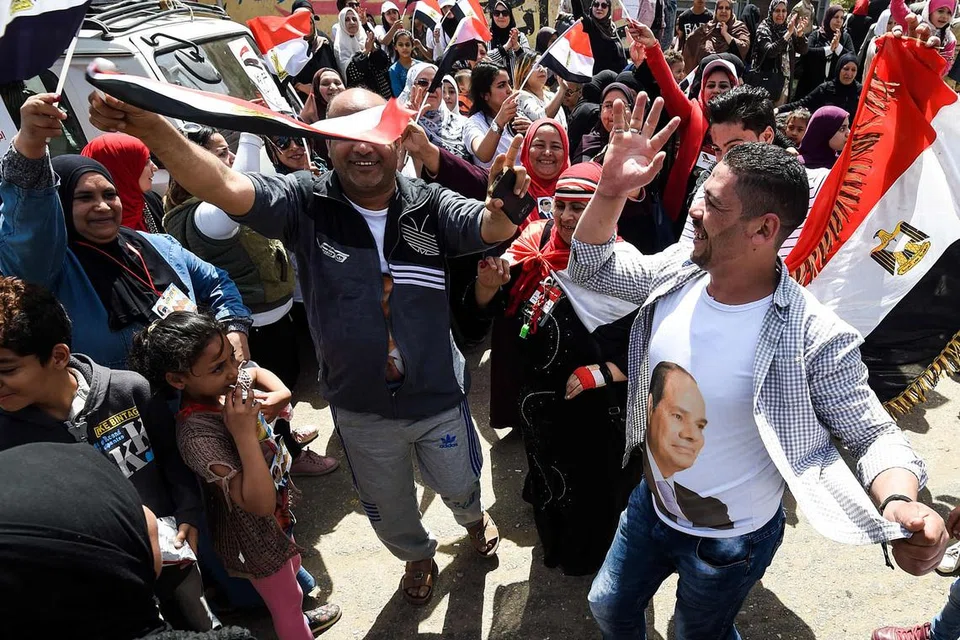 SOKONGAN MELUAS: Rakyat Mesir menari, dengan membawa bendera negara dan memakai kemeja-T tertera gambar Presiden Abdel Fattah al-Sisi, di luar sebuah pusat mengundi di al-Omraniya di Giza semasa pilihan raya pada 26 Mac. Encik Fattah popular dalam kalangan rakyatnya. - Foto AFP