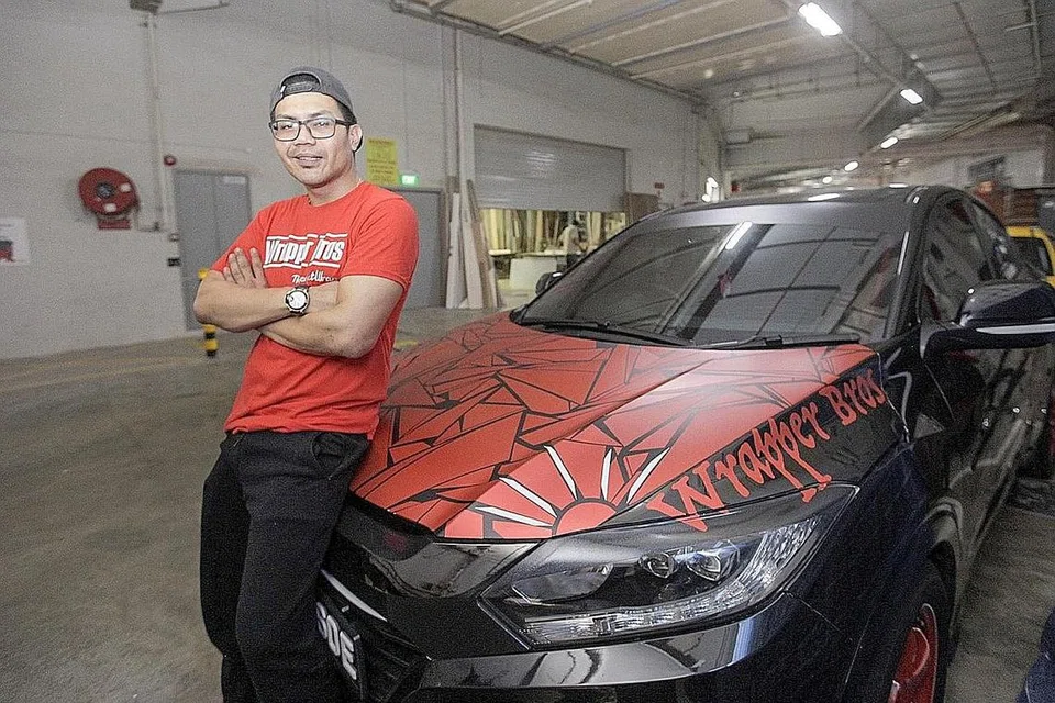 DAYA KREATIF: Encik Ismail Ng gunakan daya kreativitinya sendiri bagi membuat dan menghasilkan rekaan pelekat kereta seperti kereta hitam di belakangnya yang diberi hiasan pelekat berwarna merah. - Foto BH oleh IQBAL FAIZAL