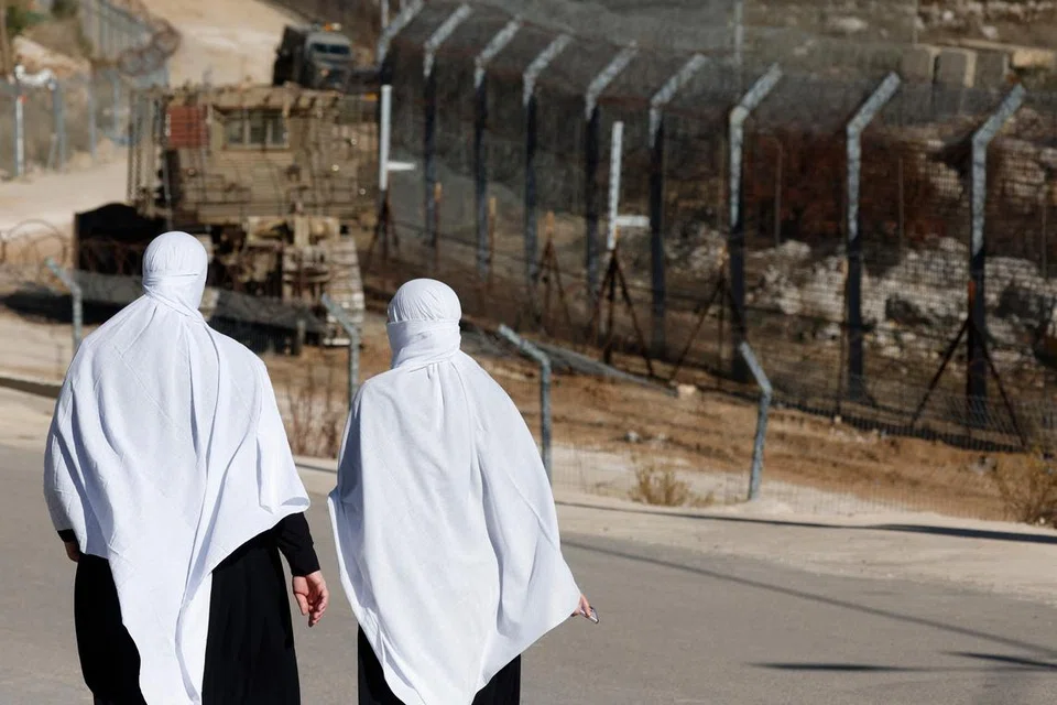 Wanita keturunan Druze berjalan berhampiran pagar menuju ke zon penampan di bawah pengawasan Pertubuhan Bangsa-Bangsa Bersatu  (PBB), yang memisahkan pasukan Israel dengan Syria di Bukit Golan, pada 15 Disember.