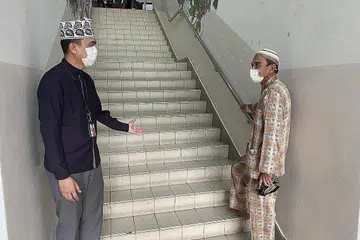 PERLU MENAIKI TANGGA KE ARAS DUA: Pengurus Masjid Darul Makmur, Ustaz Ruhaizan Abdullah (kiri) menyambut kehadiran jemaah, Encik Noor Mohamed sewaktu beliau menaiki tangga untuk ke aras dua. - Foto MASJID DARUL MAKMUR.