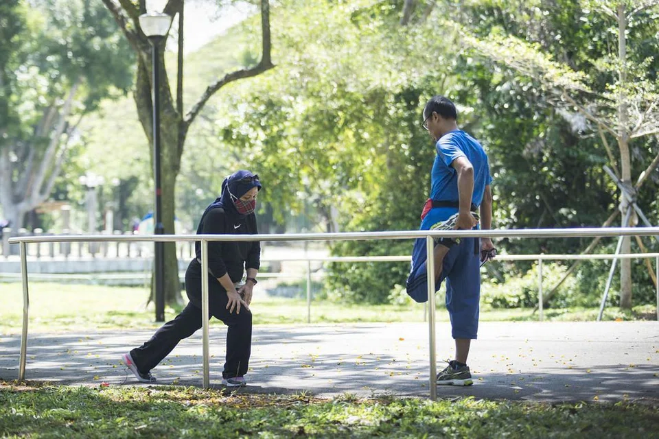 PATUHI JARAK SELAMAT: Cik Lita Rosnita (memakai pelitup, gambar kiri) dan suaminya Encik Anto Harry bersenam di Pasir Ris Park sambil mematuhi jarak selamat antara satu sama lain. - Foto BH oleh HARITH MUSTAFFA