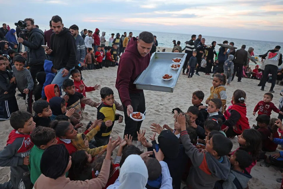 Encik Hamada Shaqoura, yang dahulunya seorang ‘blogger’ makanan, mengagihkan makanan kepada kanak-kanak selepas menyediakan hidangan untuk mangsa kehilangan tempat tinggal di Khan Yunis, selatan Jaluran Gaza pada 16 Januari 2025. 