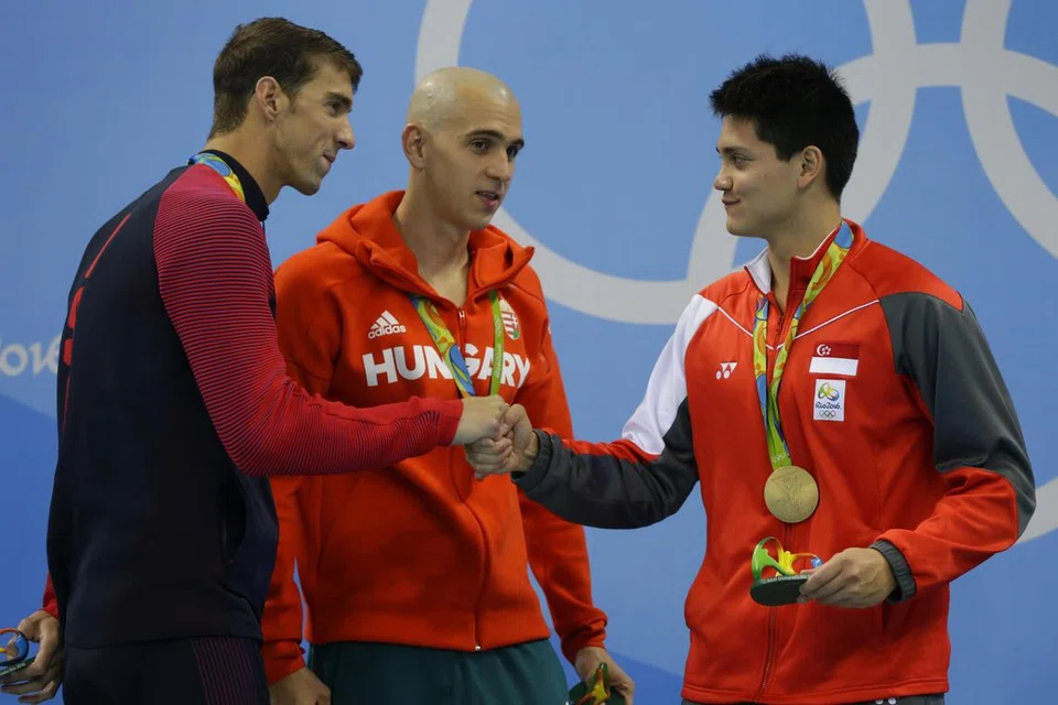 Michael Phelps (kiri) dari Amerika Syarikat mengucapkan tahniah kepada Joseph Schooling (kanan) dari Singapura, sementara Laszlo Cseh (tengah) dari Hungary melihat, di podium selepas final acara 100m kuak kupu-kupu lelaki di Sukan Olimpik Rio 2016 di Stadium Akuatik Olimpik, Rio de Janeiro, Brazil, pada 12 Ogos 2016. Schooling mengalahkan Phelps dan Cseh untuk memenangi pingat emas dalam acara tersebut.