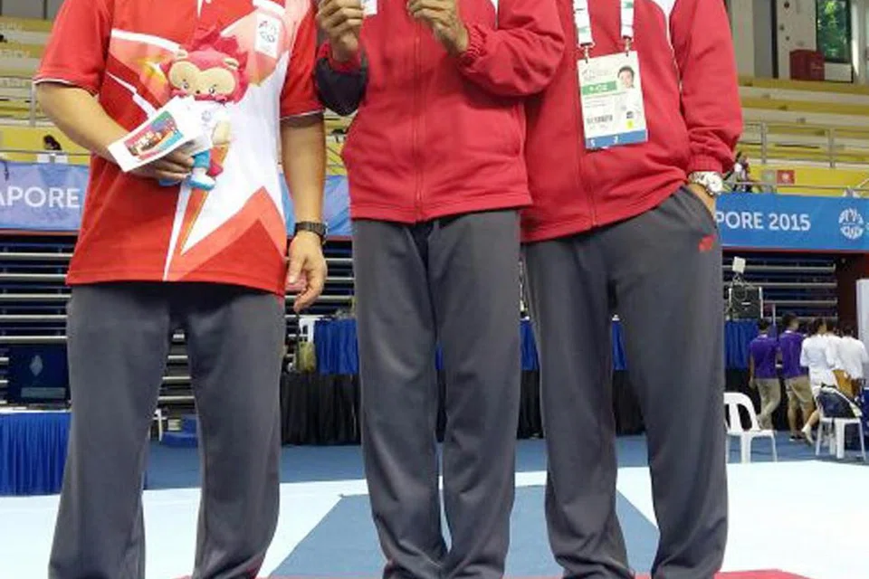 Aizat (tengah) bergambar bersama dua pingat gangsa Sukan SEA 2015 yang dimenanginya. Bersama beliau ialah jurulatihnya ketika itu, Lin Zhenqiu (kiri), dan pegawai gimnastik negara, Janssen Ong.