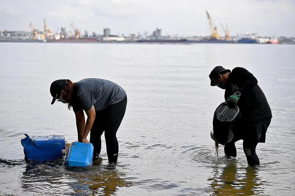 PANTAI BERSIH: Relawan SG Beach Warriors, Cik Nurasylah (kiri) dan Encik Irsyad, membersihkan tong air yang tertimbus dalam pasir untuk dikumpulkan sebagai sampah yang dikutip dalam sesi pembersihan pantai. - Foto BM oleh LIM YAOHUI