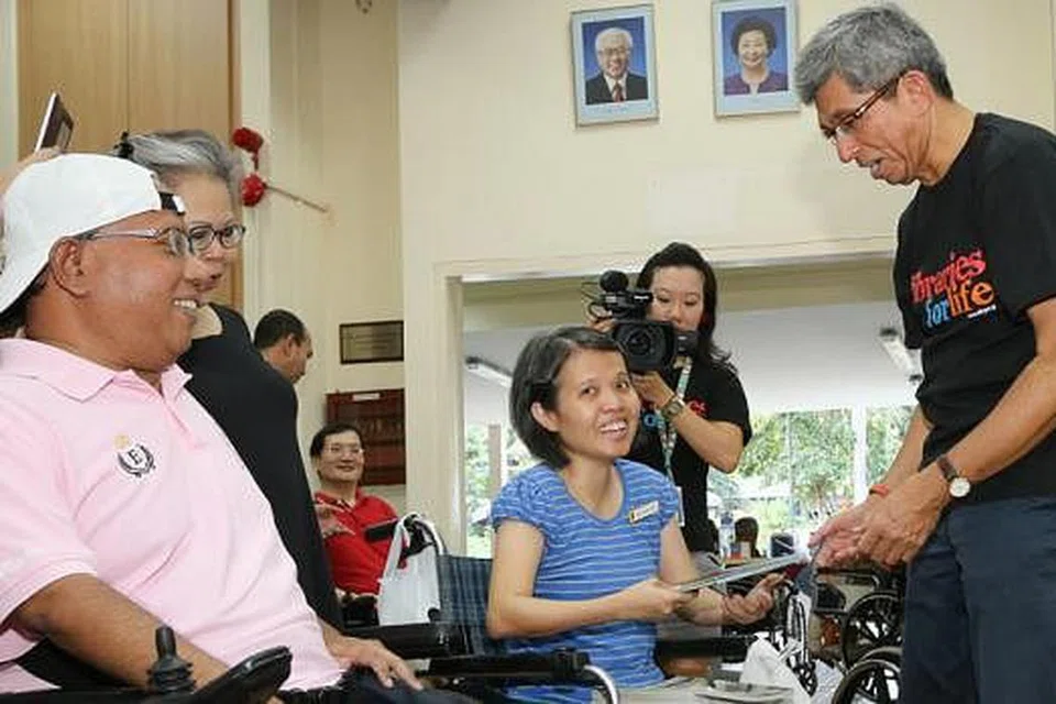 UNTUK SEMUA: Dr Yaacob Ibrahim (berdiri) bersama sukarelawan inisiatif 'Project Deliver Me' berinteraksi dan memberi beberapa buku kepada penghuni Singapore Cheshire Home semasa kunjungan mereka semalam. - Foto NLB