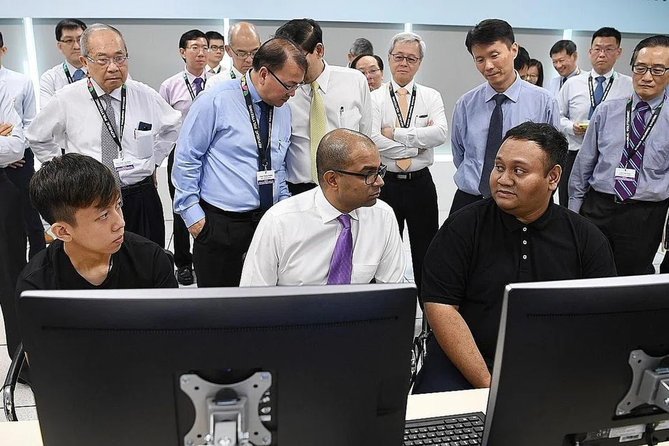KERJASAMA KUKUHKAN KEMAHIRAN TENAGA KERJA: Encik Syahirul (kanan, berbaju hitam) dan Encik Javier Ng, pelajar RP, (kiri, juga berbaju hitam) mengongsi pengalaman pembelajaran mereka bersama Dr Puthucheary (tengah, duduk) di Makmal Pengurusan Operasi Kereta Api RP-LTA. - Foto BH oleh KHALID BABA
