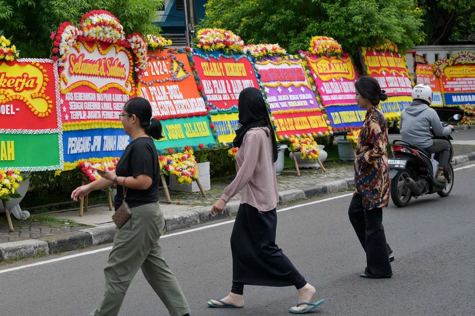 Pejalan kaki melintasi papan ucapan tahniah kepada calon pemimpin Jakarta, Encik Pramono Anung dan Encik Rano Karno, yang setakat ini mendahului keputusan pilihan raya Gabenor Jakarta berdasarkan kiraan pantas, di Jakarta pada 29 November. 