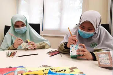 KARYA SENI: Pelajar menengah dua MAI, Salwa Sanaullah Khan (kiri) dan Nur Sumayyah Mohammad Zaki (kanan) menggunakan bahan mewarna kering - pensel warna, krayon dan penanda untuk mereka karya seni Cube Art. - Foto MAI