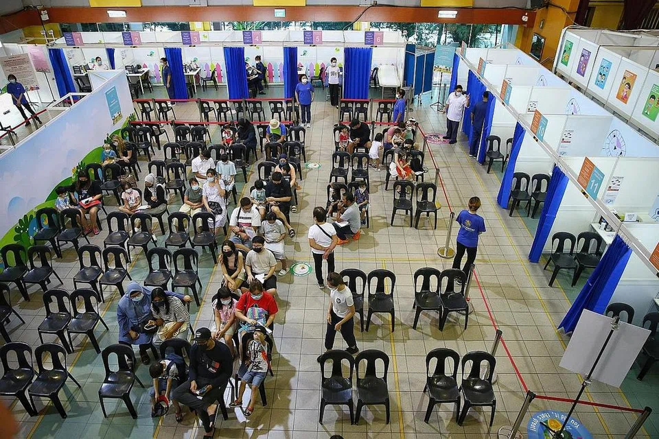 TUNGGU GILIRAN: Ibu bapa dan anak mereka sedang menunggu giliran untuk mendapatkan suntikan vaksin Moderna Spikevax di Kelab Masyarakat Sembawang semalam. - Foto BH oleh FELINE LIM