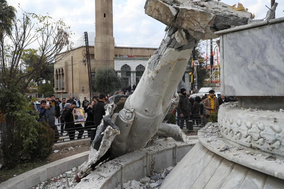 Orang ramai berkerumun di sekeliling patung mantan Presiden Syria Hafez al-Assad yang musnah selepas pemberontak mengumumkan bahawa mereka telah menggulingkan Presiden Bashar al-Assad pada 8 Disember. 