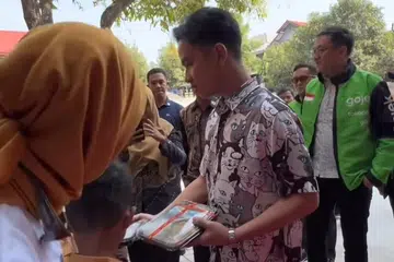 Bakal Naib Presiden, Encik Gibran Rakabuming Raka, membahagikan makanan percuma kepada pelajar sekolah sedang Indonesia akan melancarkan ribuan dapur di seluruh negara bermula 2025.