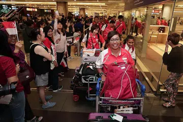 WIRA NEGARA: Atlit memanah wanita negara, Nur Syahidah Alim (depan), selamat pulang ke tanah air bersama kontinjen negara yang bertanding di APG di Jakarta dengan disambut meriah oleh anggota keluarga dan penyokong di Terminal 2 Lapangan Terbang Changi semalam. - Foto BH oleh KELVIN CHNG