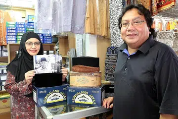 TERUSKAN WARISAN BAPA: Cik Isneli (kiri), sambil memegang gambar Allahyarham Haji Baharuddin Sulaiman, pemilik asal kedai songkok Singalang Jaya, berharap dapat meneruskan perniagaan bapanya itu. Bersamanya ialah suami, Encik Hashmy, yang pernah membantu arwah mengendalikan kedai itu dahulu. - Foto FAKHRURADZI ISMAIL