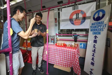 Seorang pekerja pengangkutan menghulurkan secawan kopi kepada orang awam di dalam Coffee Bus.