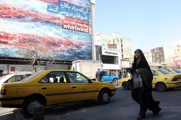Seorang wanita Iran berjalan melepasi papan iklan anti-Amerika Syarikat di Tehran, Iran, 25 Februari 2026. Amerika Syarikat dan Iran dijadual menyambung pusingan ketiga rundingan nuklear penting di Geneva.