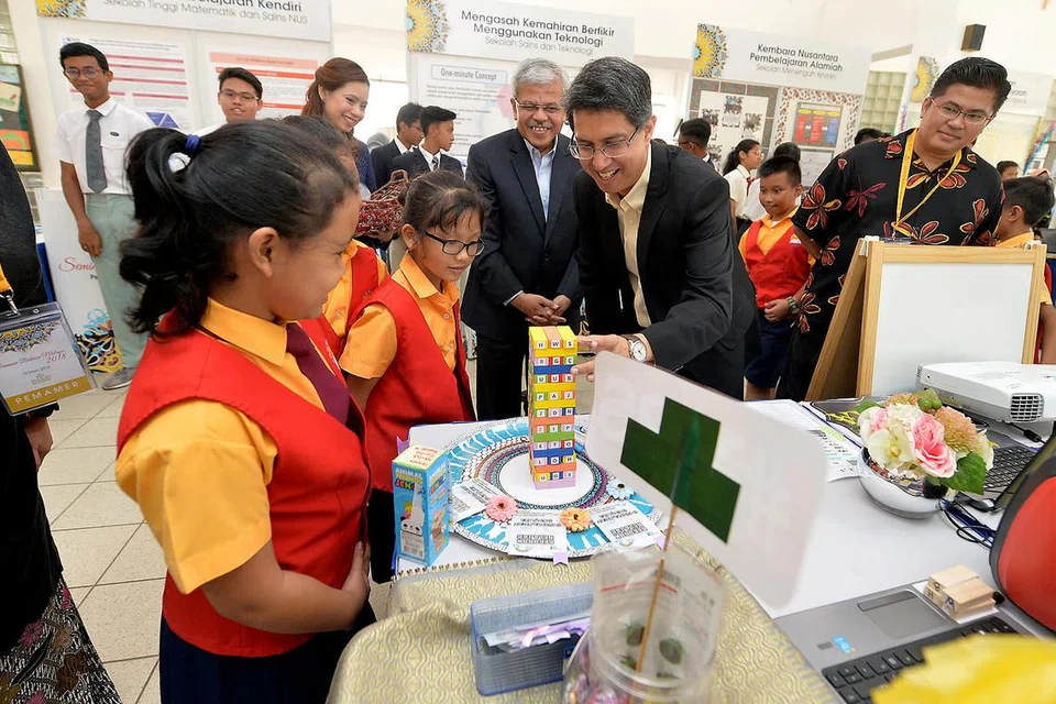CARA KREATIF BELAJAR BAHASA: Dr Muhammad Faishal Ibrahim kelihatan berbual mesra dengan murid-murid di gerai Sekolah Rendah Yumin mengenai permainan bongkah kayu dalam pembelajaran imbuhan. Beliau bersama Pengarah Pusat Bahasa Melayu Singapura (MLCS), Encik Mohamed Noh Daipi (tiga dari kanan), di Seminar Bahasa Melayu 2018 di Bishan semalam. - Foto BH oleh M.O SALLEH.