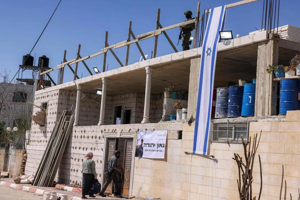 Pendatang Yahudi memasuki rumah milik warga Palestin yang telah dirampas di Tebing Barat dan meletakkan bendera Israel, dengan  diperhatikan askar Israel.