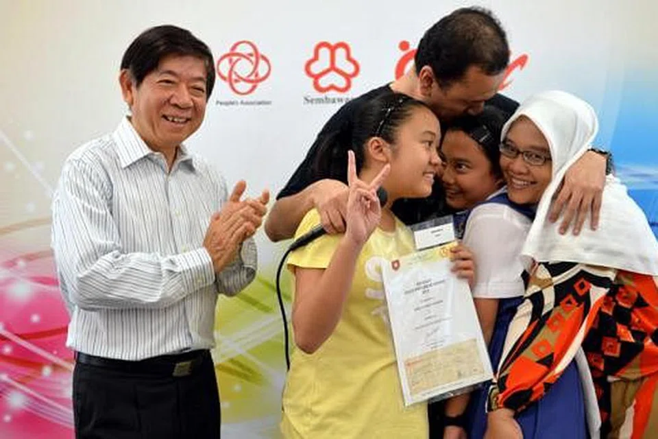 GEMBIRA TAK TERHINGGA: Encik Huszairy, Cik Er (bertudung) dan Arianna (berbaju kuning) memeluk Ardelia sambil diperhatikan Encik Khaw di atas pentas setelah beliau diberi Anugerah Edusave. - Foto M.O. SALLEH