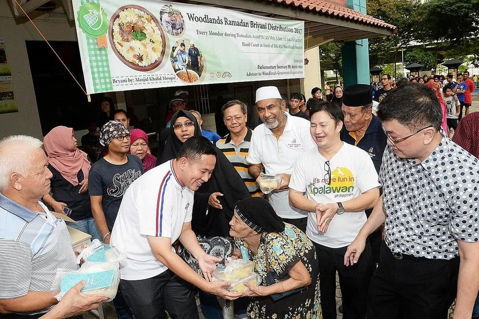 AGIH BERIANI: Encik Amrin mengagih nasi beriani yang disiapkan oleh Masjid Khalid kepada penduduk kawasan Woodlands sebelum waktu berbuka. Turut serta ialah pengerusi Masjid Khalid, Haji Allaudin Mohamed (bersongkok putih). - Foto JOHARI RAHMAT