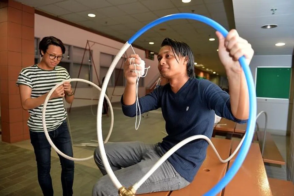 MENYIAPKAN PEMASANGAN: Penuntut diploma jurusan rekaan ruang dari Politeknik Nanyang, (dari kiri) Encik Muhammad Mirza Ramlan dan Encik Muhammad Khuraihan Amron, melilitkan tali di gelung hula yang akan menjadi 'kaki' sotong gurita bagi pemasangan rekaan mereka yang bernama 'Tako Man'. 