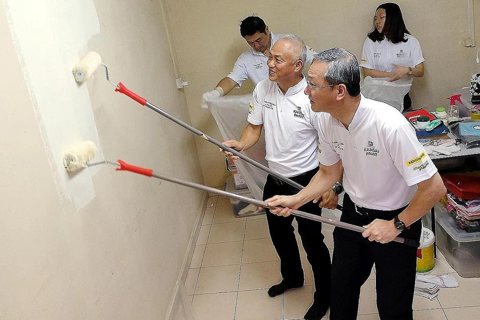 CAT CEGAH NYAMUK: Encik Tan (depan) bersama Ketua pegawai operasi, Kansai Paint Singapura, Encik Richard Leong, gigih mengecat semula dinding salah sebuah rumah yang dipilih semalam. - Foto KHALID BABA