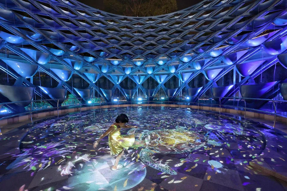 Seorang kanak-kanak perempuan cuba berinteraksi dengan unjuran cahaya di Symphony Streams di Sentosa Sensoryscape.