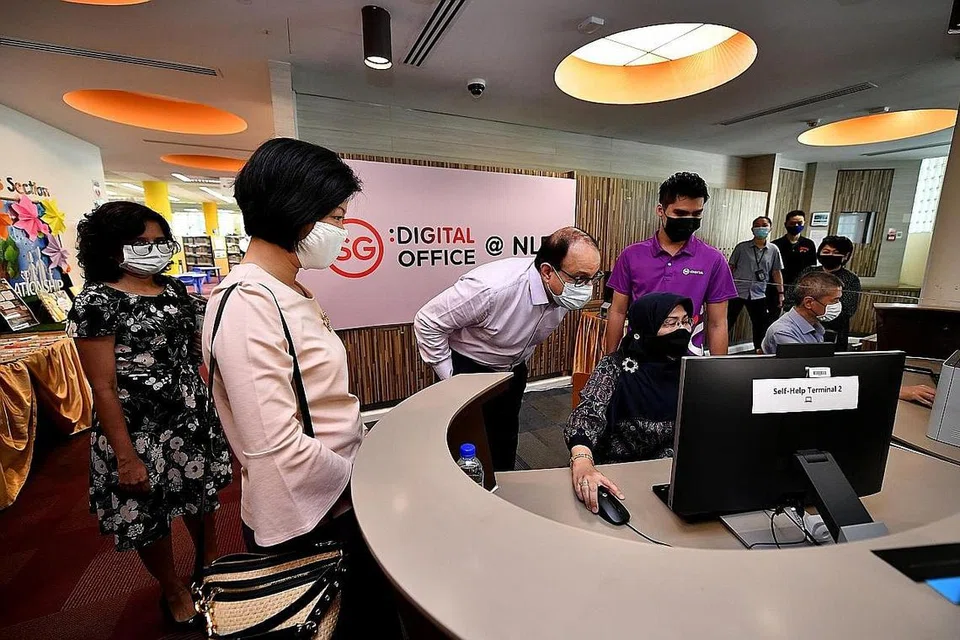 KHIDMAT DIGITAL: Encik Iswaran, Menteri Negara Kanan (Perhubungan dan Penerangan merangkap Pembangunan Negara) Sim Ann lihat pesara Cik Siti Hajar Hamzah, 64 tahun, guna khidmat digital pemerintah di Perpustakaan Awam Geylang East. - Foto BH oleh LIM YAOHUI