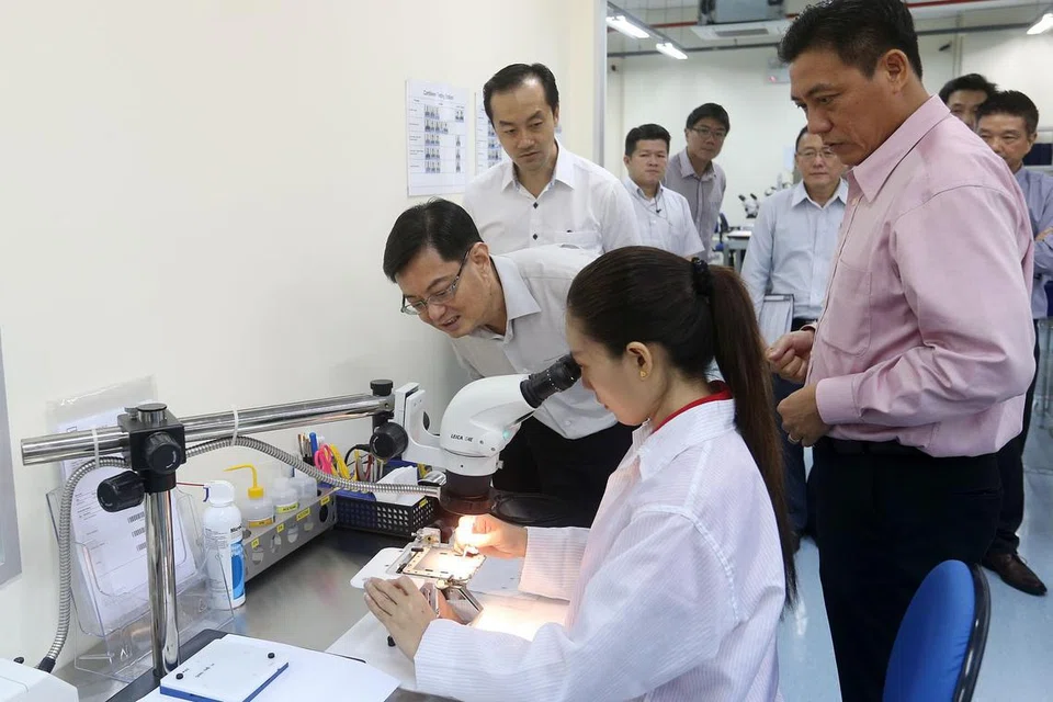PRODUK CANGGIH: Encik Heng Swee Keat (sedang tunduk)bersama Dr Koh Poh Koon (dua dari kiri)meninjau proses kerja di syarikat Feinmetall yang menghasilkan kad ujian wafer. - Foto ZAOBAO