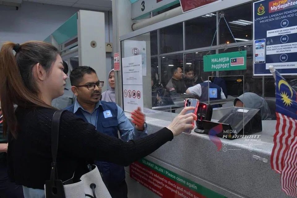 Seorang wanita warga Malaysia (kiri) mencuba penggunaan kod respons pantas (QR) untuk pelepasan Jabatan Imigresen di Kompleks Kastam, Imigresen dan Kuarantin (CIQ) di Kompleks Sultan Abu Bakar (KSAB) Johor Bahru dengan bantuan pegawai imigresen. 