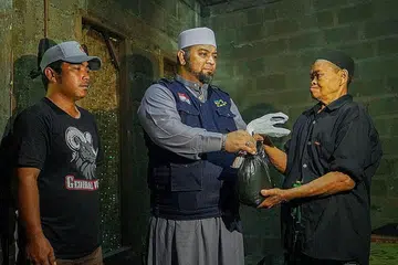 BERKONGSI REZEKI: Kebahagiaan penerima daging korban yang hanya mampu dinikmati hanya setahun sekali, bersama Pengarah IbadahSg, Ustaz Mohmed Firdaus Masruhen (tengah). - Foto IBADAHSG PTE LTD