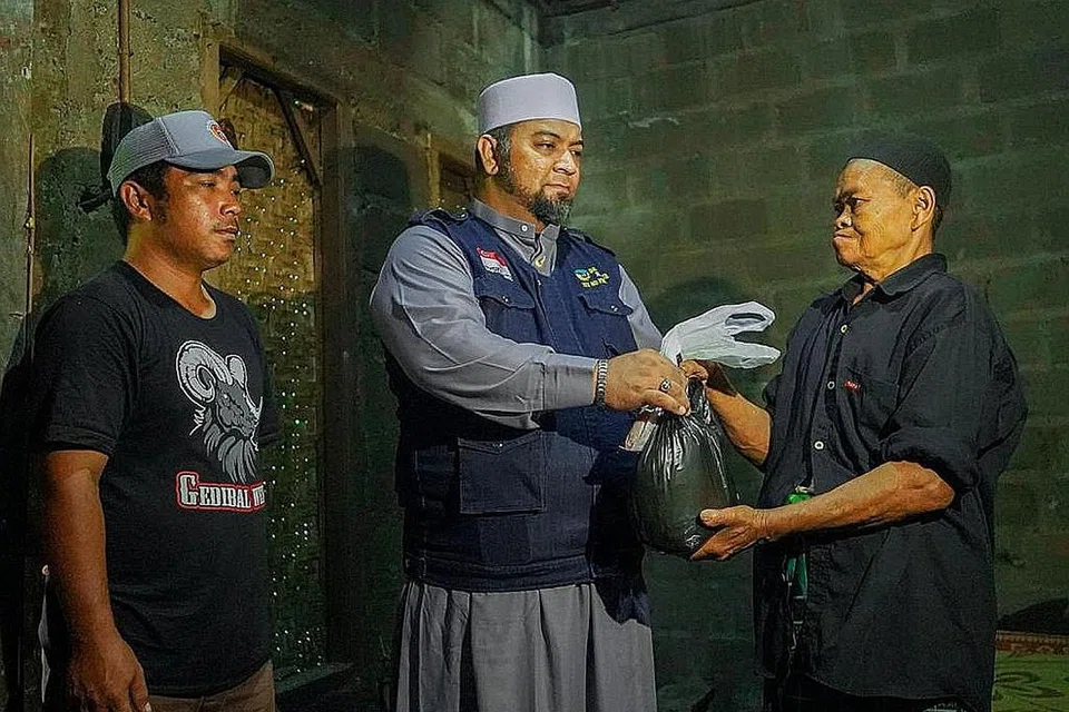BERKONGSI REZEKI: Kebahagiaan penerima daging korban yang hanya mampu dinikmati hanya setahun sekali, bersama Pengarah IbadahSg, Ustaz Mohmed Firdaus Masruhen (tengah). - Foto IBADAHSG PTE LTD