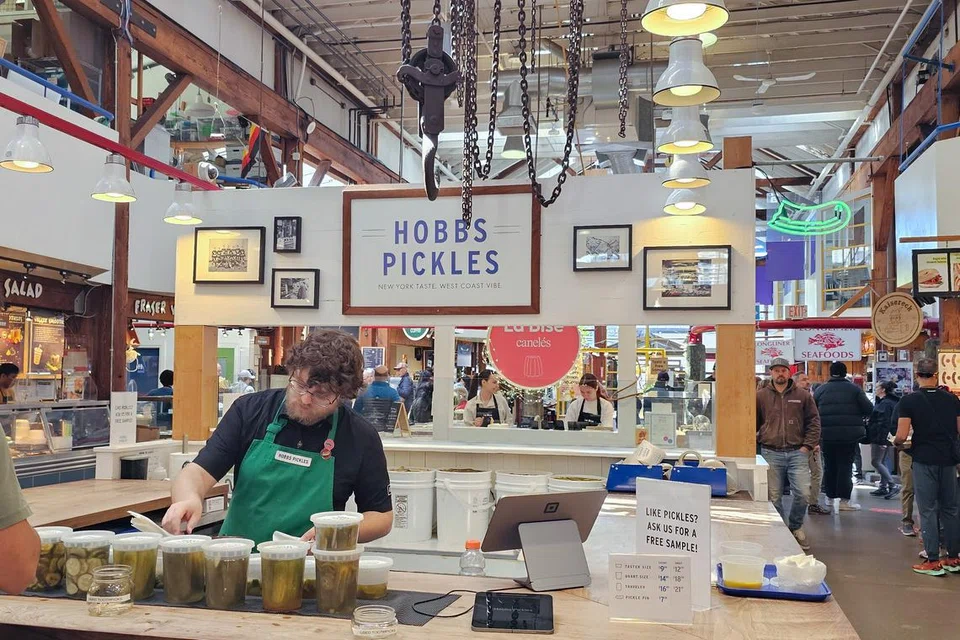 Penjual di Hobbs Pickles sedang melayani pelanggan dengan pelbagai jenis jeruk segar di pasar awam Granville Island.