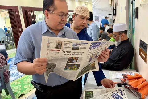 Eksekutif Teknologi Maklumat, Encik Del Rasouli Abdul Rashid (kiri), membaca akhbar Berita Harian (BH) yang diterimanya di Masjid Muhajirin di Braddell Road pada 15 Mei.
