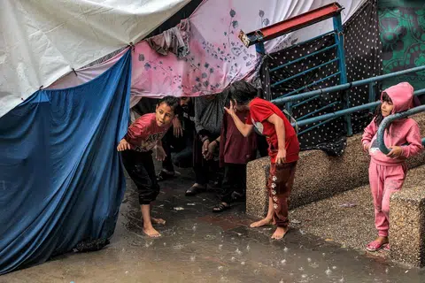 HUJAN LEBAT: Kanak-kanak berlindung daripada hujan di bawah khemah di sebuah sekolah yang dikendalikan oleh Agensi Bantuan dan Kerja Menyelamat Pertubuhan Bangsa-Bangsa Bersatu (UNRWA) di Rafah, di selatan Semenanjung Gaza, pada 14 November.