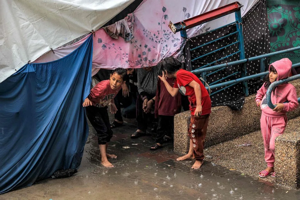 HUJAN LEBAT: Kanak-kanak berlindung daripada hujan di bawah khemah di sebuah sekolah yang dikendalikan oleh Agensi Bantuan dan Kerja Menyelamat Pertubuhan Bangsa-Bangsa Bersatu (UNRWA) di Rafah, di selatan Semenanjung Gaza, pada 14 November.
