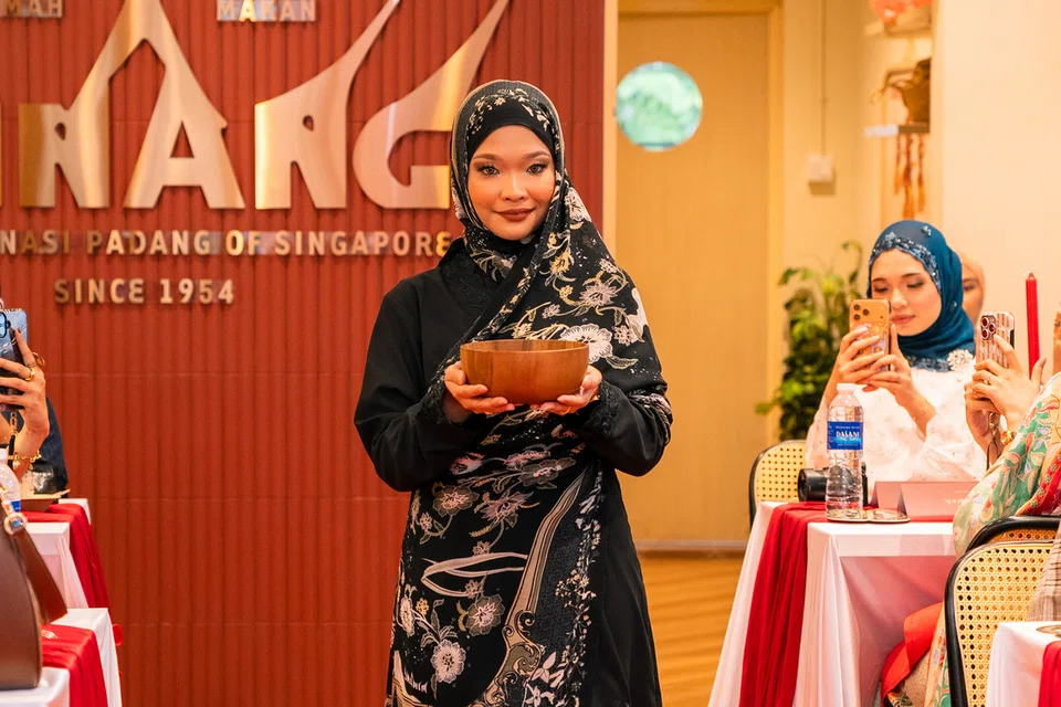 Seorang model sedang memperagakan tudung Sajian Singapura sambil membawa pulut hitam semasa acara pelancaran pada 30 Julai.