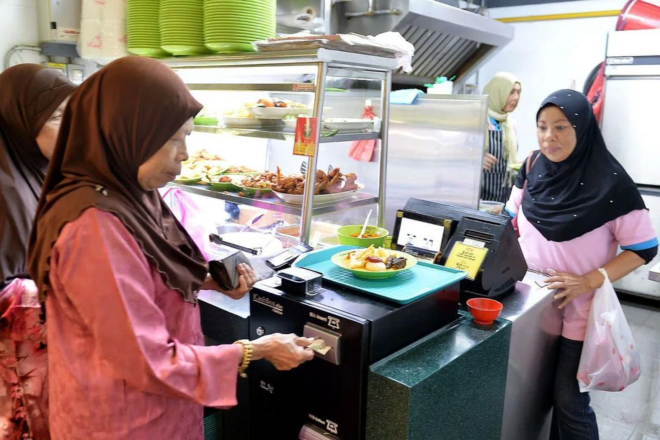 PELBAGAI PILIHAN: Orang ramai boleh memilih pelbagai masakan Melayu termasuk yang diusahakan oleh Cik Sabariah Haron (tengah) yang memasukkan duit ke dalam sistem bayaran iCashBox yang digunakan di semua gerai di pusat makanan di Our Tampines Hub. - Foto fail 