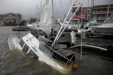 HAMPIR KARAM: (Gambar atas) Sebuah bot hampir tenggelam dan dimasuki air setelah kawasan Pensacola, Florida, dilanda Taufan Sally. Seorang pemandu sedang meredah banjir di bandar Pensacola, Florida. - Foto-foto REUTERS, AFP
