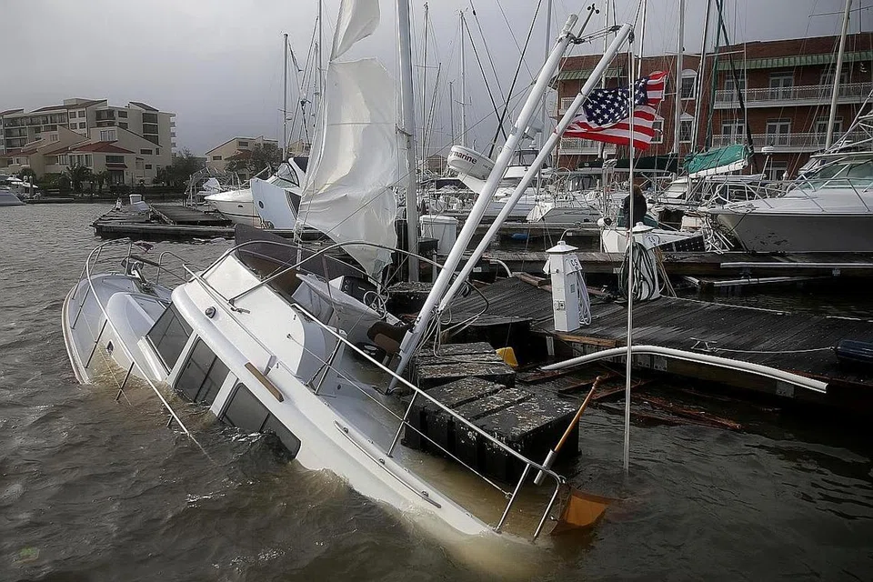 HAMPIR KARAM: (Gambar atas) Sebuah bot hampir tenggelam dan dimasuki air setelah kawasan Pensacola, Florida, dilanda Taufan Sally. Seorang pemandu sedang meredah banjir di bandar Pensacola, Florida. - Foto-foto REUTERS, AFP