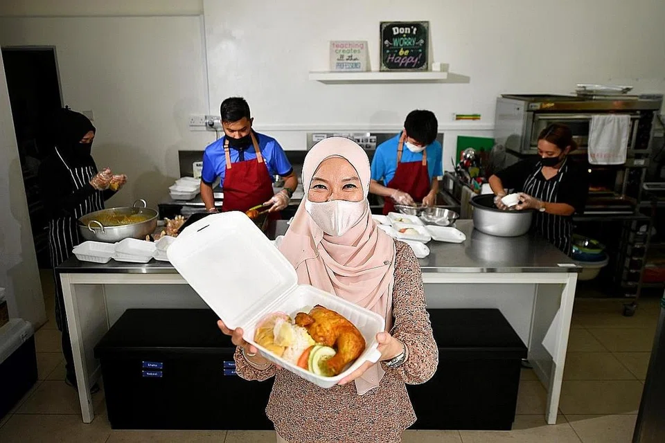 HIDANGAN SEGAR BAGI KELUARGA ISTIMEWA: Cik Faraliza Zainal menunjukkan sebungkus makanan yang akan diberikan kepada keluarga berpendapatan rendah yang mempunyai kanak-kanak berkeperluan khas. Makanan-makanan itu dibungkus oleh pekerja berkeperluan khas di Ashraf's Cafe (belakang). - Foto BH oleh LIM YAOHUI